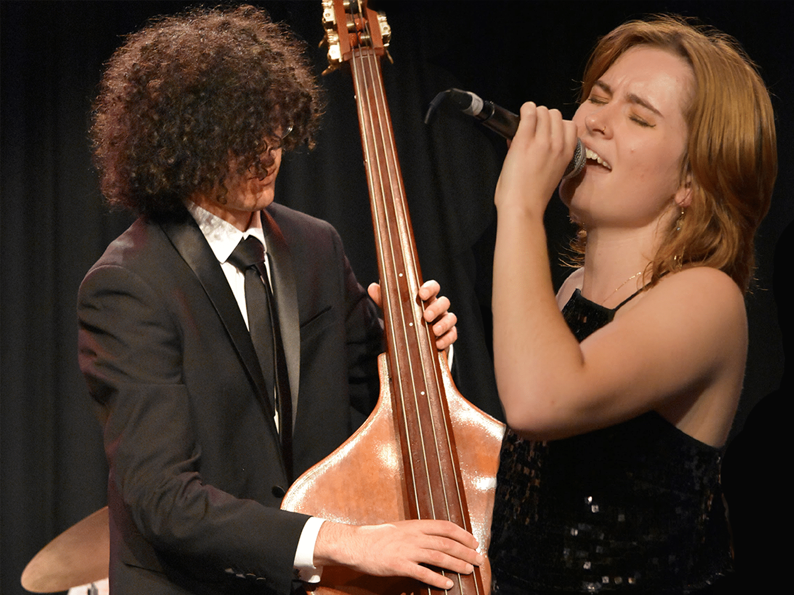 Harry playing contrabass and Imogen holding microphone, singing.