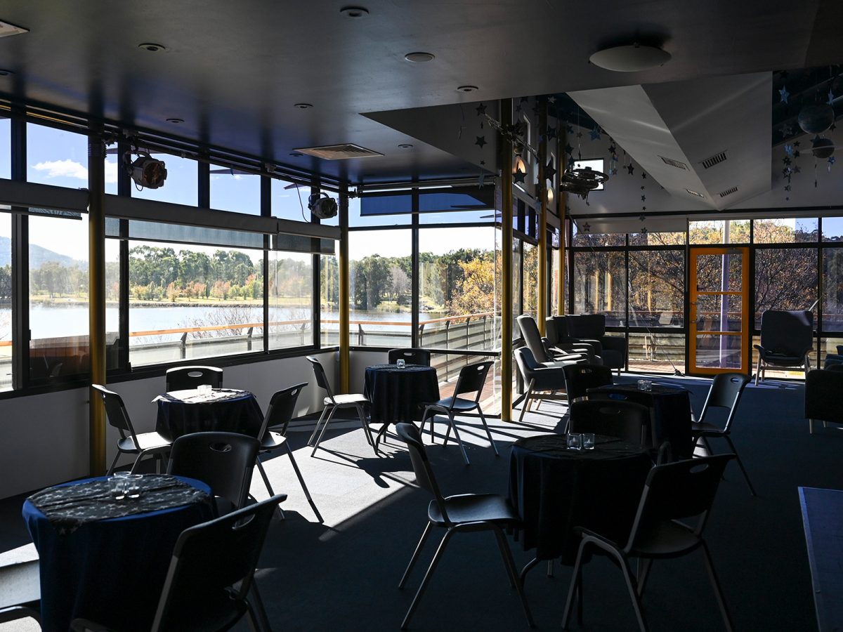 A room with round tables and chairs with large windows looking out onto a lake and trees