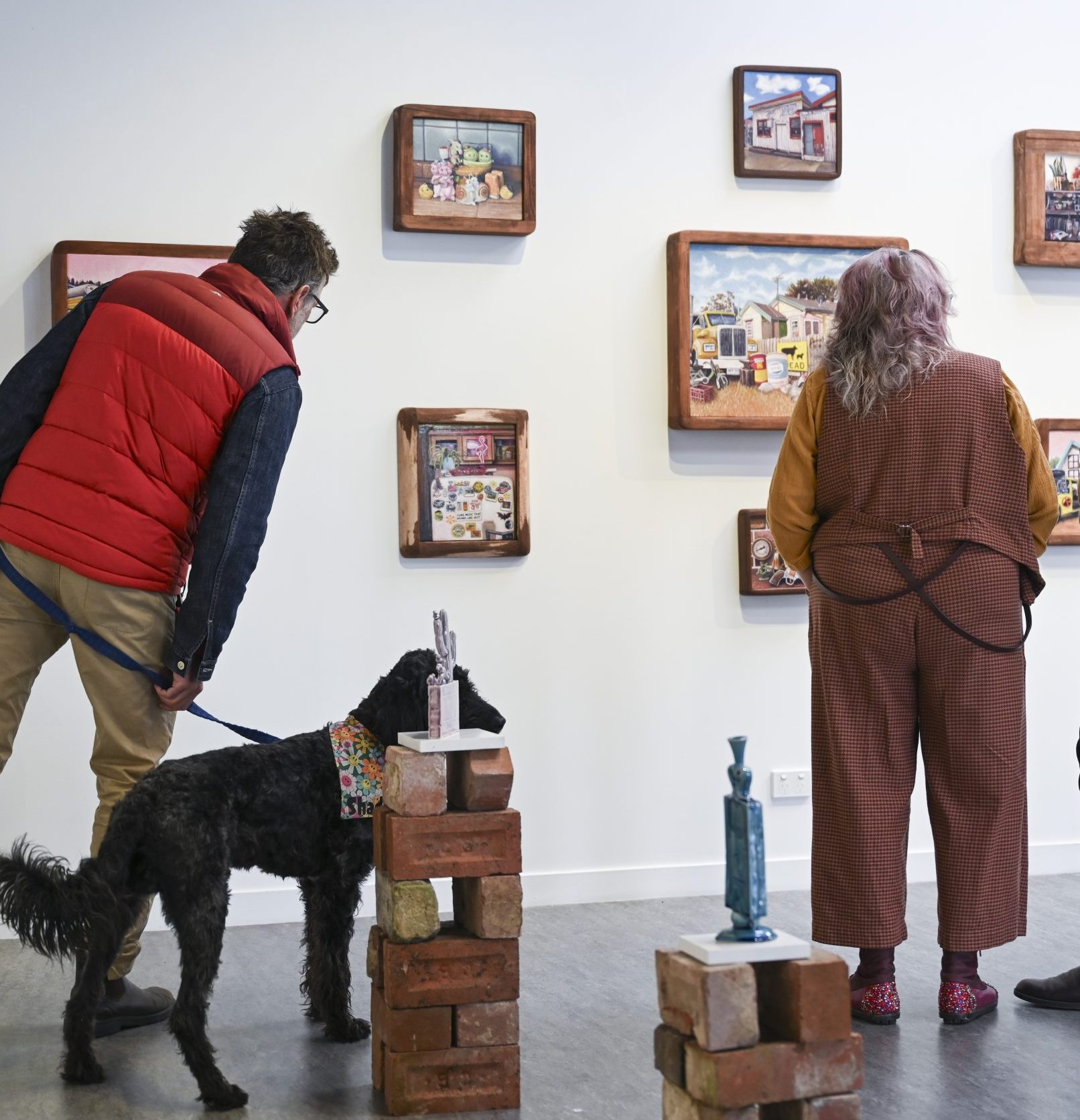 Two people and a dog enjoying the Dust Collectors exhibition at Tuggeranong Arts Centre