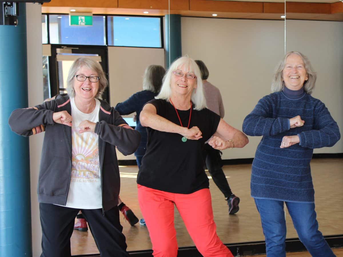 Three grey haired women in exercise clothes show off their dance moves.