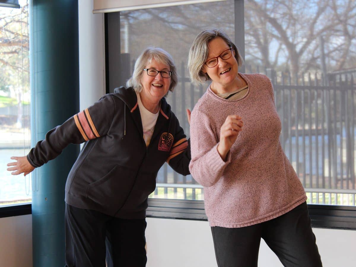 Two grey haired women in exercise clothes show off their dance moves