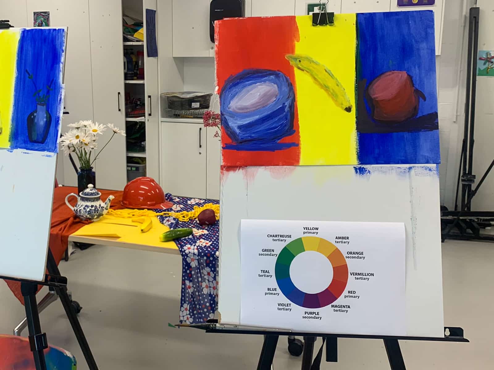 Two easels with colour studies and colour wheels on them stand in front of a still life.