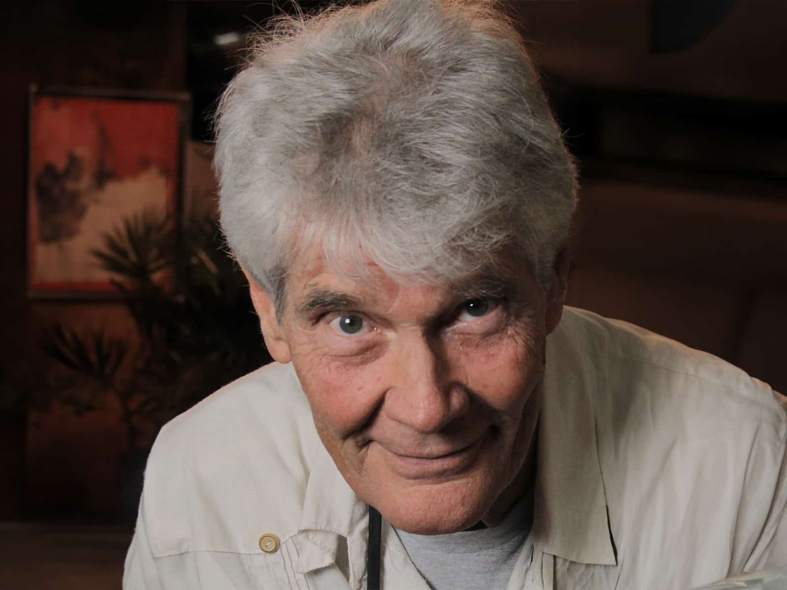 A man with grey hair in a cream shirt stares directly into the camera