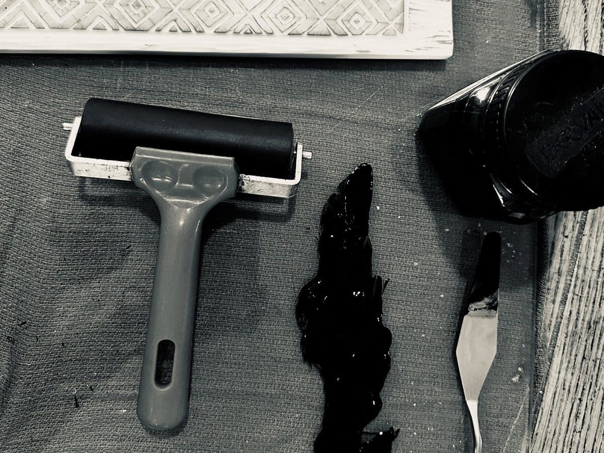 A print roller, ink, ink bottle and pallet knife lie on a hessian matt.